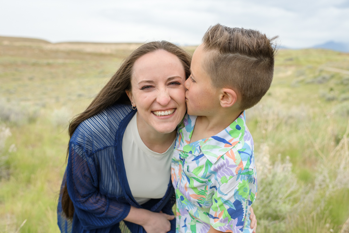 Young son kissing his mom's cheek standing in a field during a spring family session with Jodi Cornwall Photography