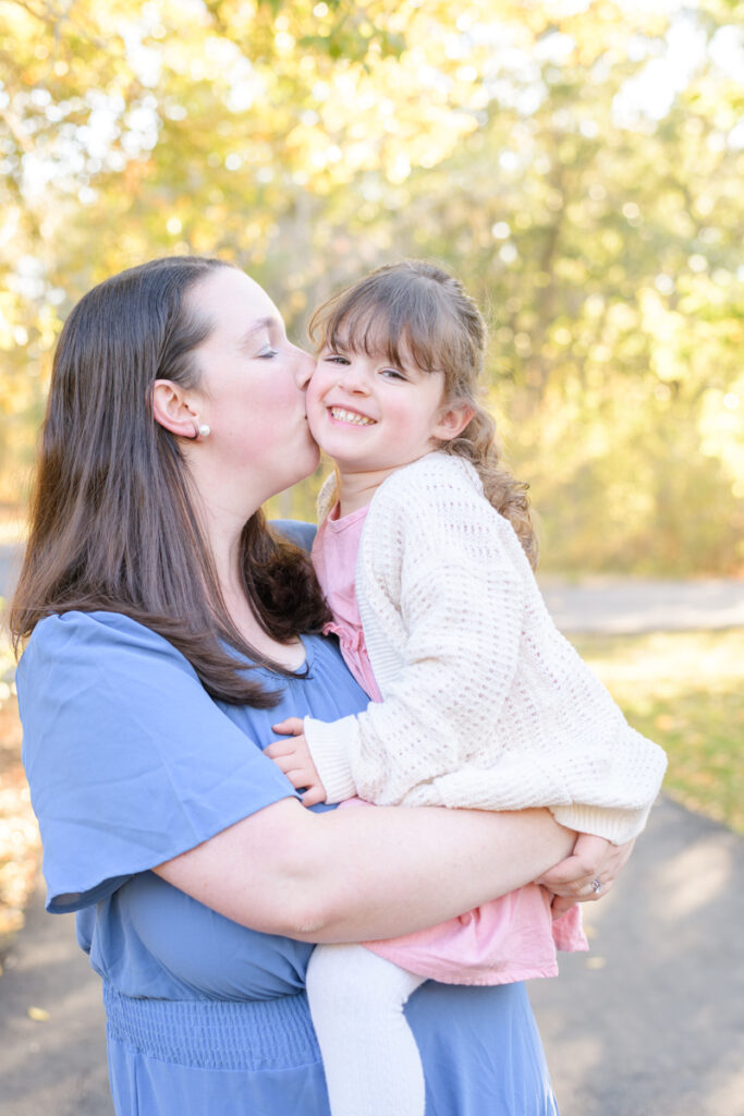 A mom kisses her young daughter's cheek during a vibrant fall family session with Jodi Cornwall Photography.