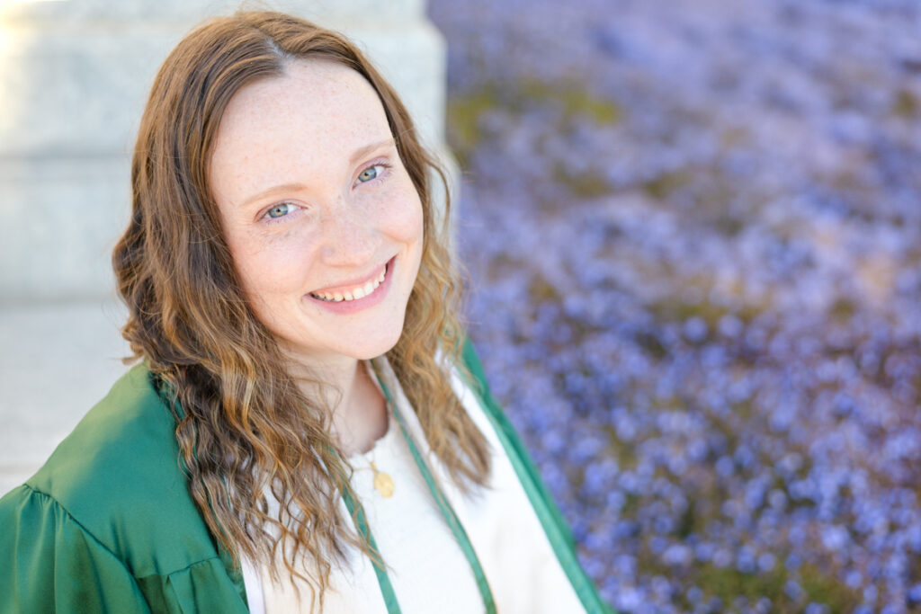 A woman smiles wearing her cap and gown during her joyful spring downtown senior session with Jodi Cornwall Photography